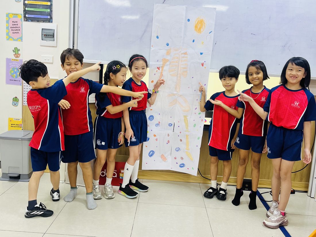 Seven students point proudly at their life-size drawing of a human skeleton, taped to the whiteboard.